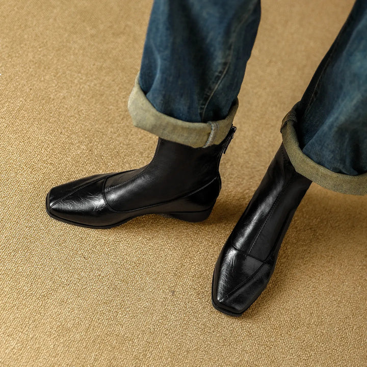 Close-up view of black leather-look Zylos square-toe ankle boots worn with cuffed denim jeans, showcasing the low block heel and back zipper detail.