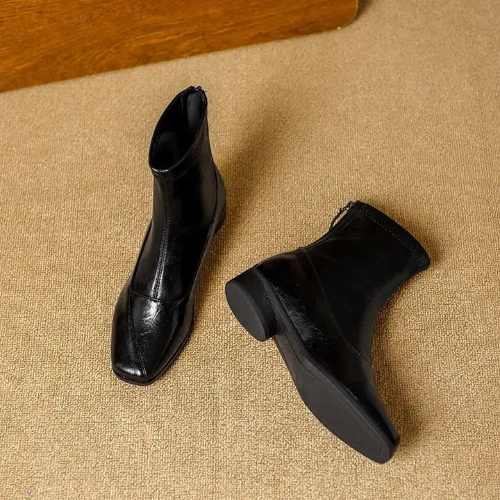 Zylos black leather-look ankle boots featuring a chic square toe and a comfortable low block heel, shown from a three-quarter angle on a textured studio floor.