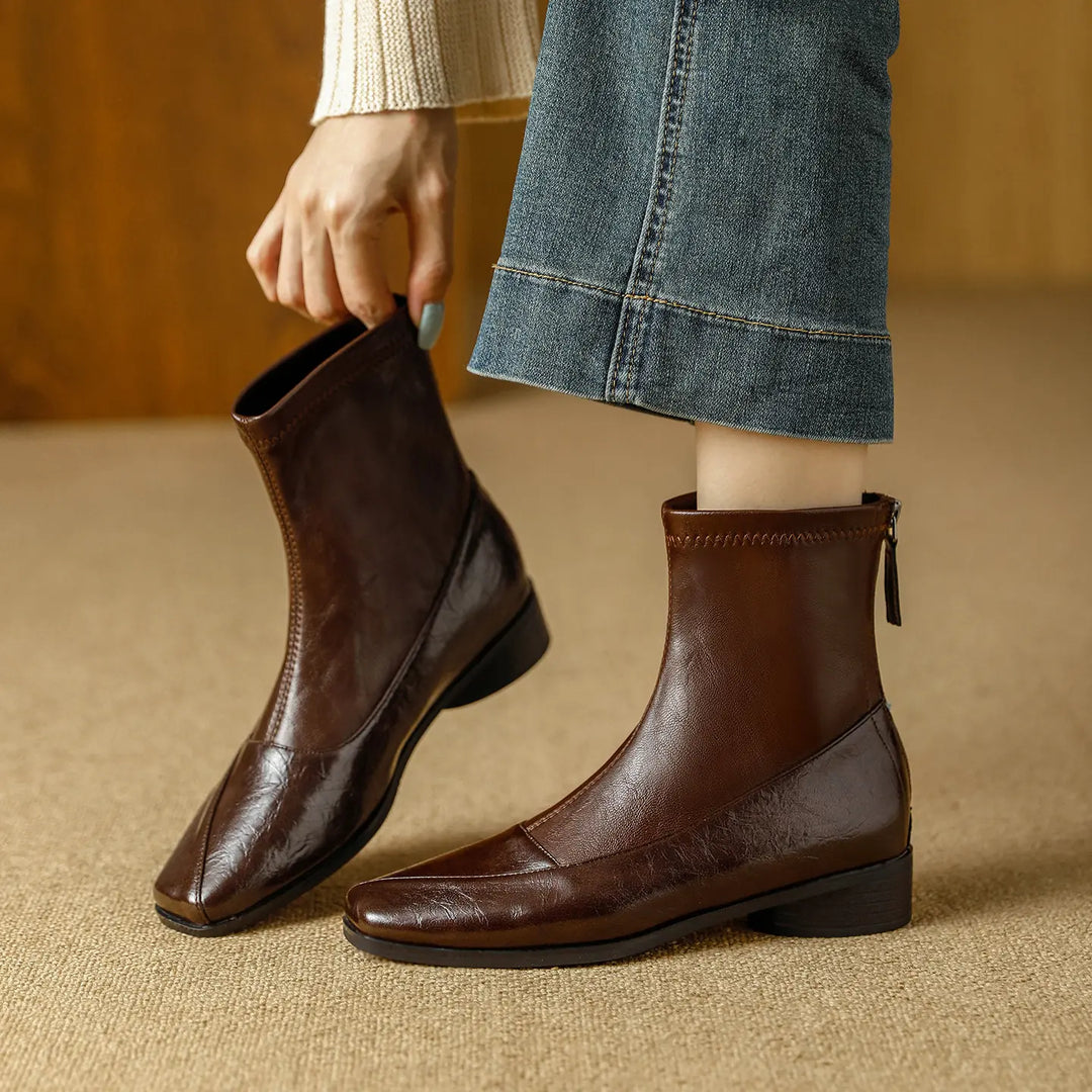 Zylos women's brown square toe ankle boots with a low block heel and back zipper, styled with denim jeans and a cream sweater.