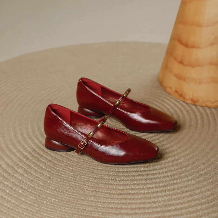 Pair of burgundy wine Zylos square toe Mary Jane shoes with low block heels and gold stud buckle straps, shown on a textured rug.