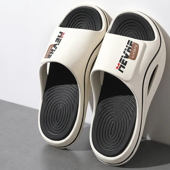Creamy off-white EVA slides with a thick sculpted sole, wave-textured footbed, and a single wide strap featuring the MEVRHE VICTORY logo in black and red.