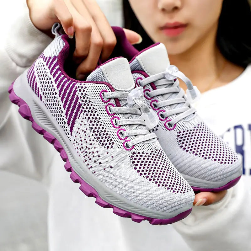 Lightweight grey and purple knit mesh trainers with a quick-lace toggle system, shown held by a person. Features a comfortable cushioned sole and breathable upper.