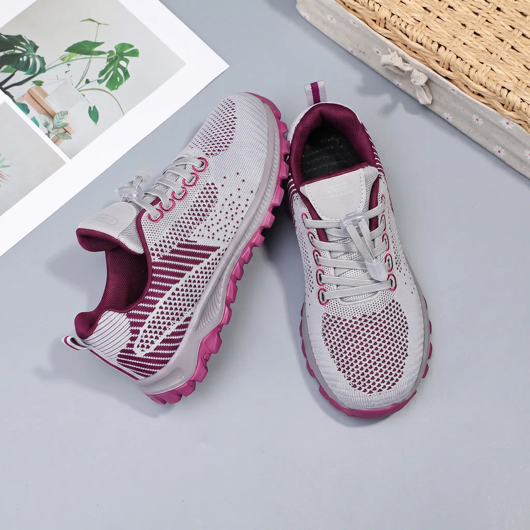 Lightweight Zylos walking trainers in grey with deep red knitted mesh uppers and a quick-lace toggle system, shown from a three-quarter angle on a studio background.