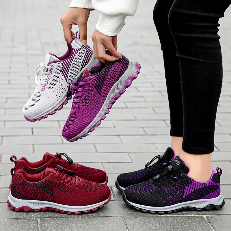 Multiple pairs of Zylos lightweight walking trainers shown in various colors including deep red, purple, and black/purple, with one pair on feet and others held. Features breathable knit upper, toggle lacing, and patterned rubber outsole.