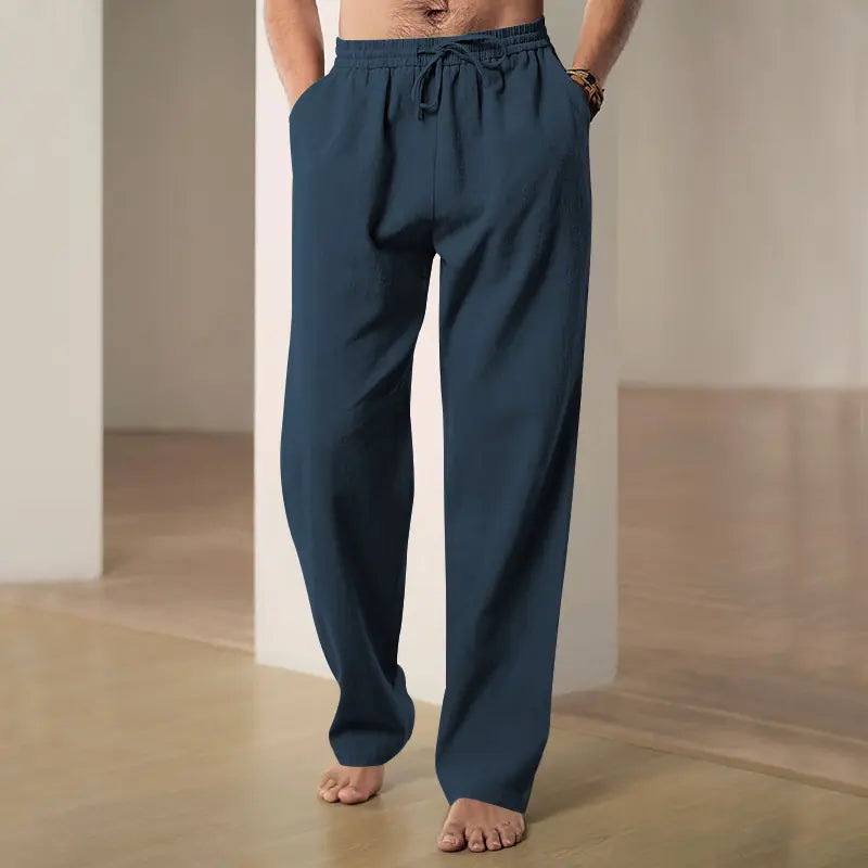 Man wearing dark blue Zylos linen-blend wide-leg trousers with a drawstring waist and side pockets, presented in a relaxed indoor setting.