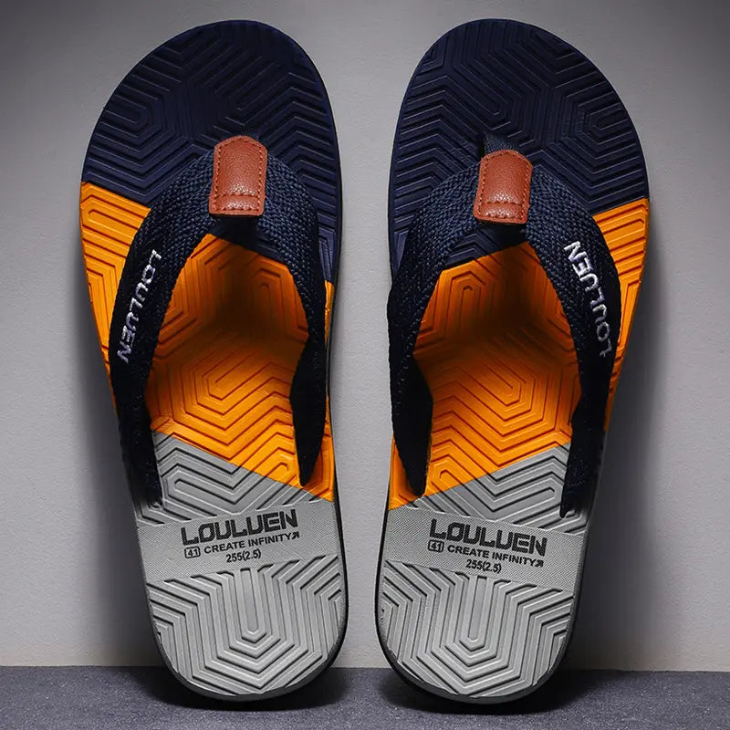 Men's Zylos flip-flops with a geometric color-blocked footbed in navy, orange, and grey, featuring woven navy straps with embroidered 'LOULUEN' logo and a textured grey/black rubber sole. Presented from a front view.
