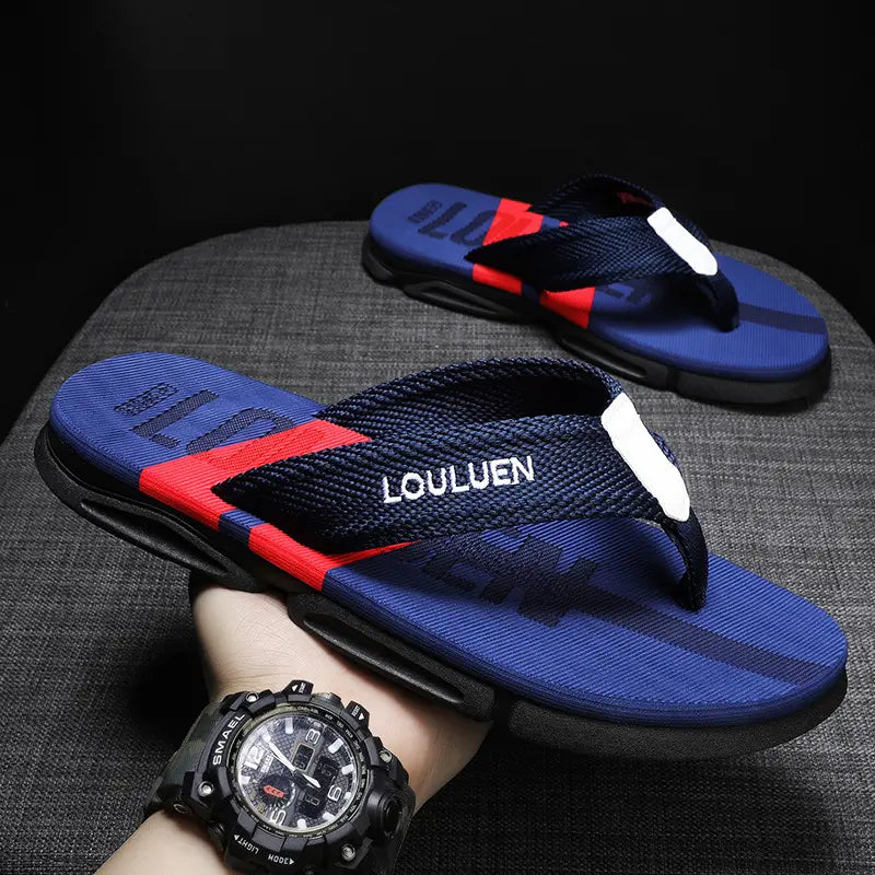 Men's navy blue Zylos designer flip-flops with a red stripe and white embroidered logo on the woven strap, presented from a three-quarter angle on a grey textured surface.