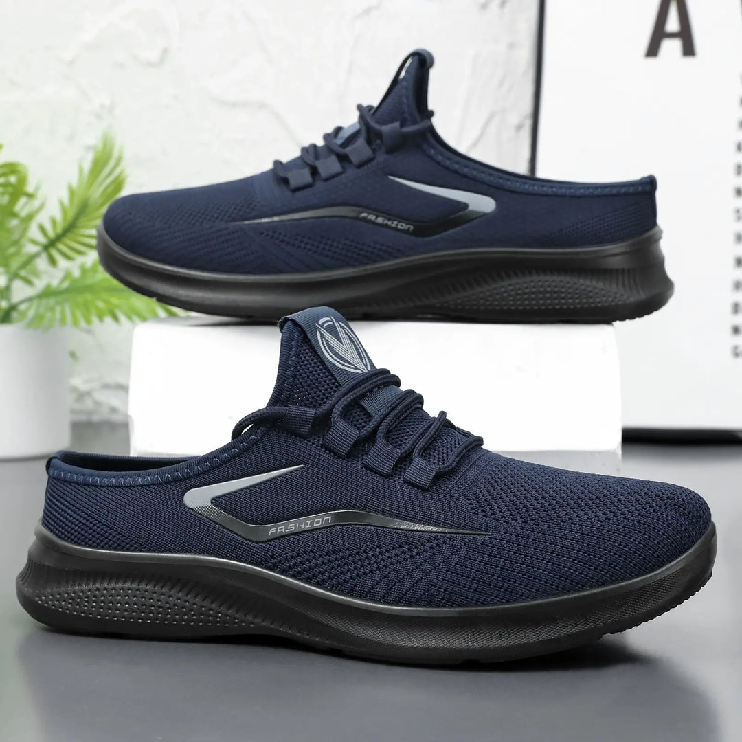Navy blue Zylos breathable comfort slip-on trainers shown from a three-quarter angle, featuring engineered mesh uppers, elastic laces, and a matte black sole with a reflective &