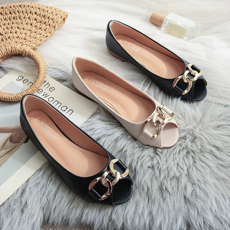 Two pairs of Zylos black peep-toe flats and one pair in apricot, each with a gold chain embellishment, laid flat on a grey rug.