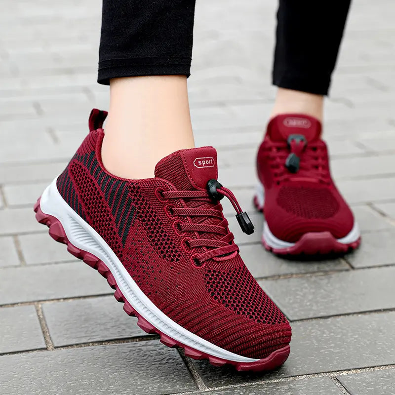 Close-up of red Zylos lightweight walking trainers worn by a person, showing the breathable knit mesh upper, toggle lacing system, and cushioned sole.