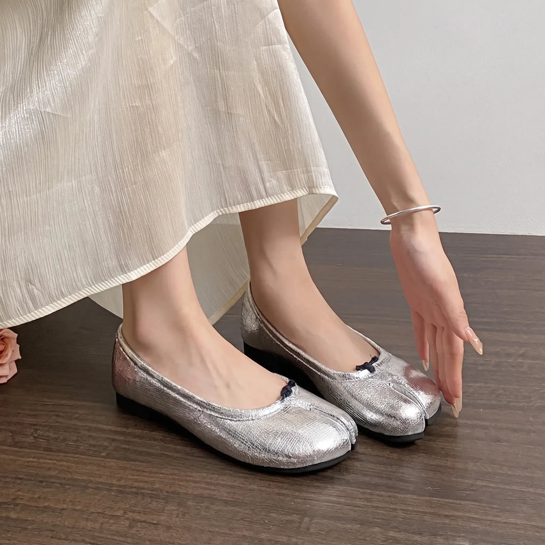 Zylos silver split-toe ballet flats worn by a woman, showcasing the unique tabi-inspired design and textured metallic finish with a low-profile round toe and flat rubber sole.