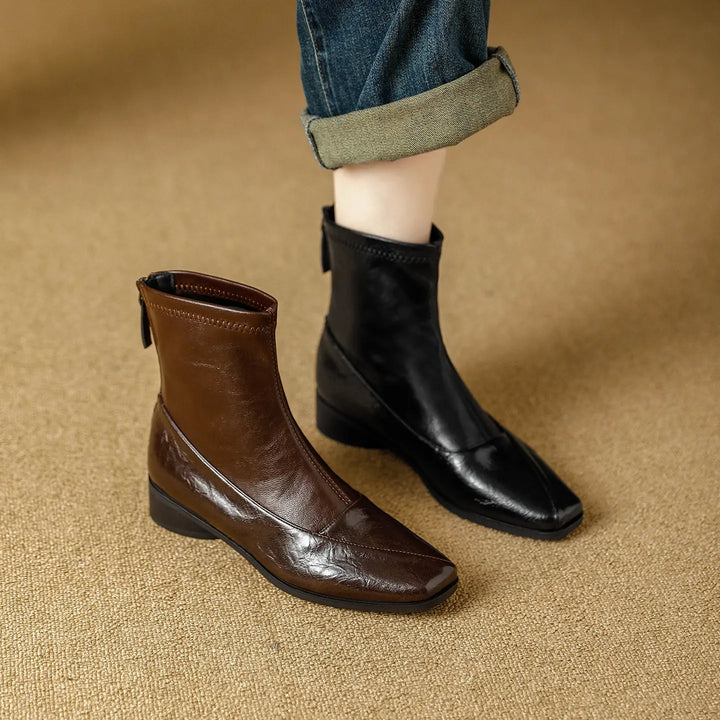 A pair of Zylos ankle boots, one brown and one black, styled with cuffed blue jeans, showcasing their square toe and low block heel.