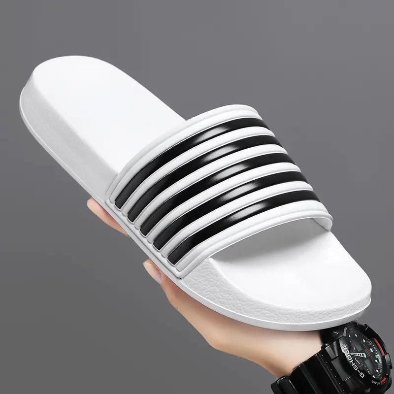 A white Zylos EVA Comfort slide with a black striped strap is held at a three-quarter angle, showcasing its thick sole and contoured footbed.