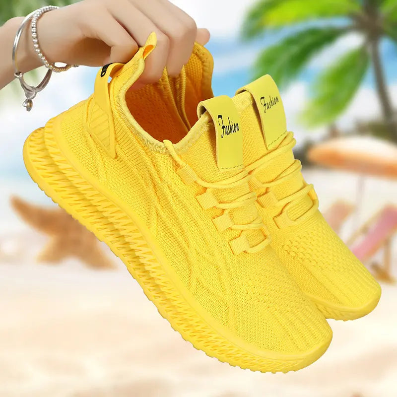 Bright yellow Zylos women's breathable casual sneakers shown in a three-quarter view with a "Fashion" label on the tongue, set against a blurred beach background with palm trees and lounge chairs.