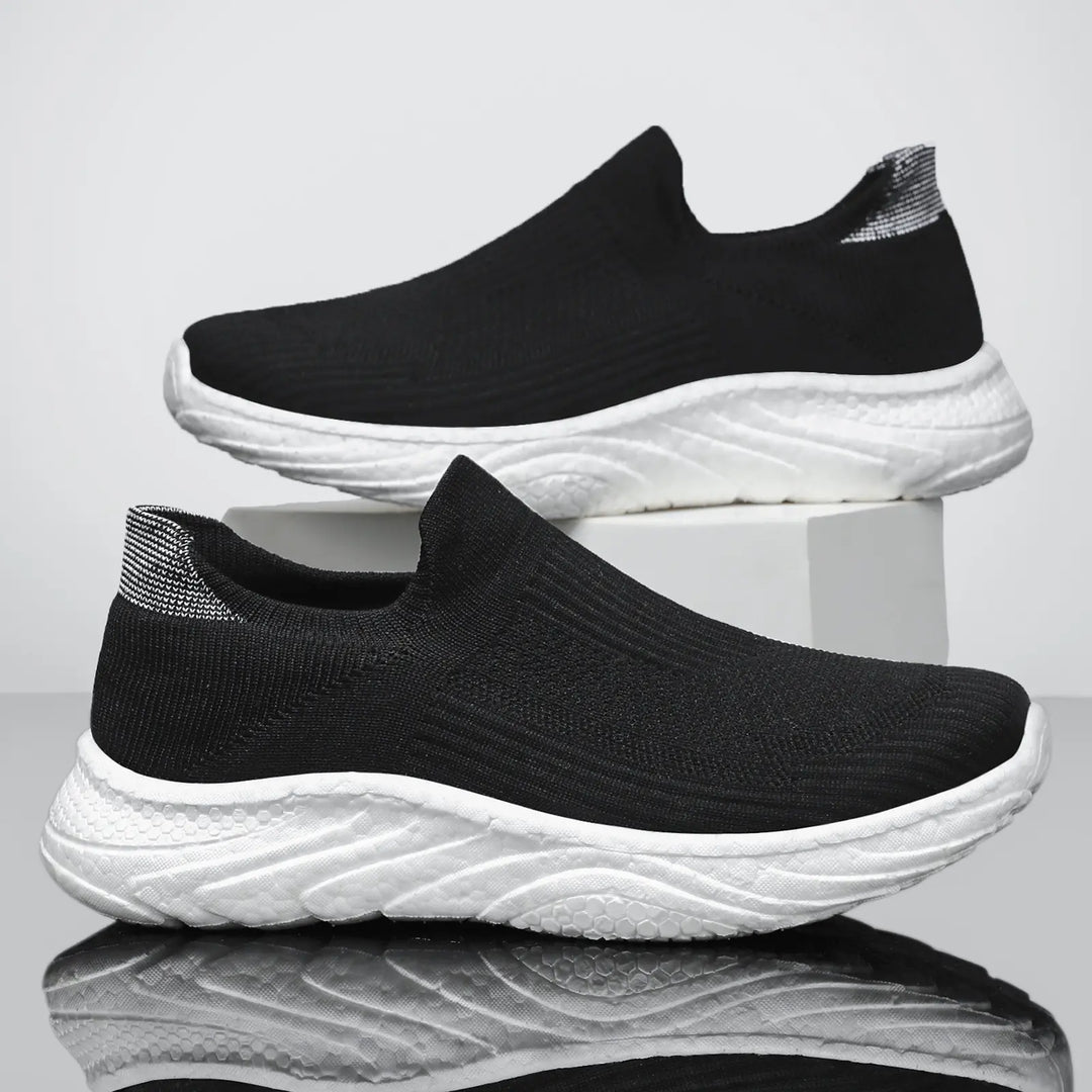Pair of black Zylpha men's casual slip-on sneakers with white sculpted soles, shown from a side profile on a white studio background.