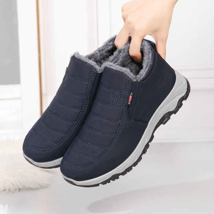 A pair of navy blue Zylpha winter boots with quilted uppers and plush faux-fur lining, held by a hand at a three-quarter angle, showcasing the &