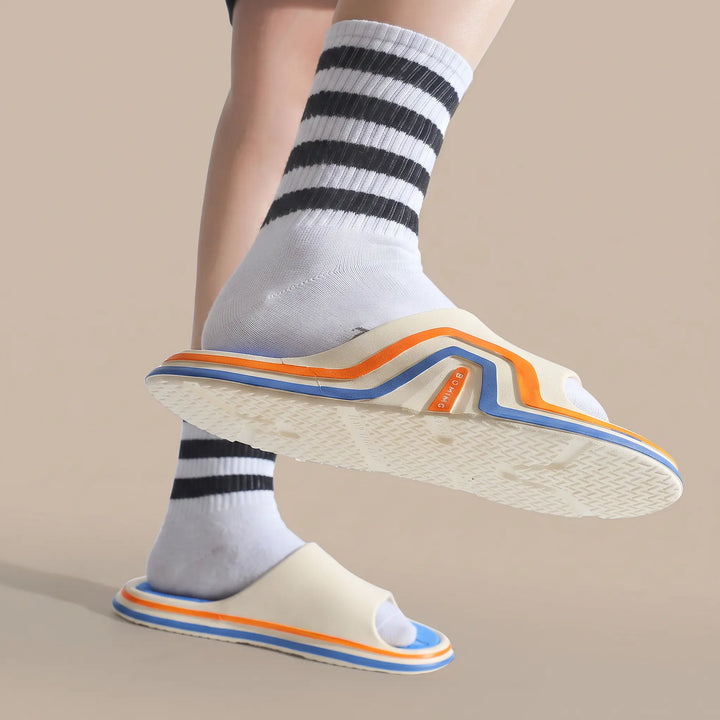 Unisex Zynex comfort slides with a white strap and a layered EVA sole featuring blue, orange, and white accents, shown on a foot wearing white socks with black stripes.