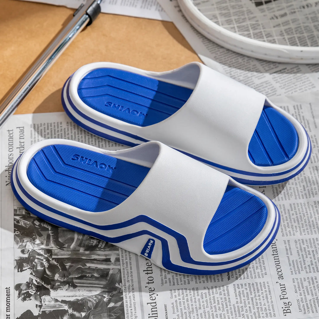 White unisex Zynex slides with blue contoured footbeds and a blue and white striped sole, shown from a three-quarter angle on a styled newspaper background.