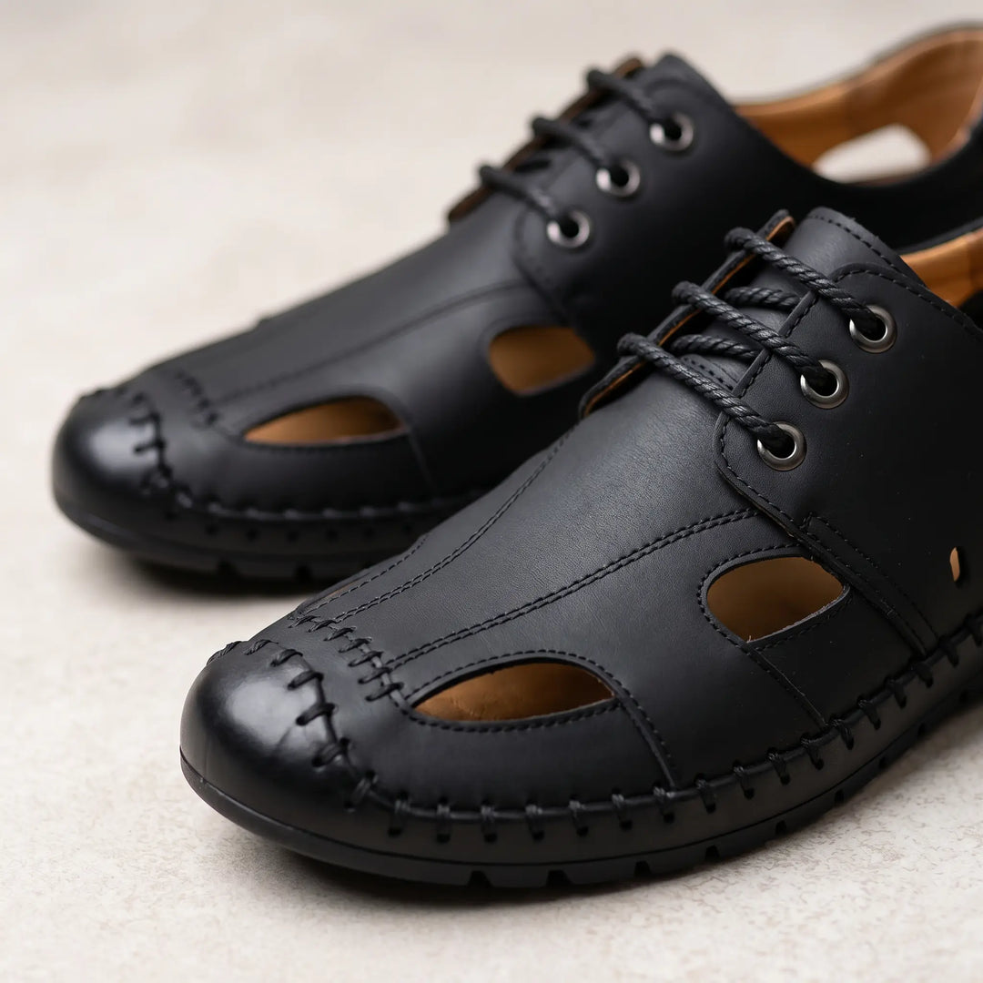 Close-up view of Zynith men's matte black leather sandals, showcasing the closed toe cap with stitched overlay, side cut-outs for breathability, and lace-up front detail.
