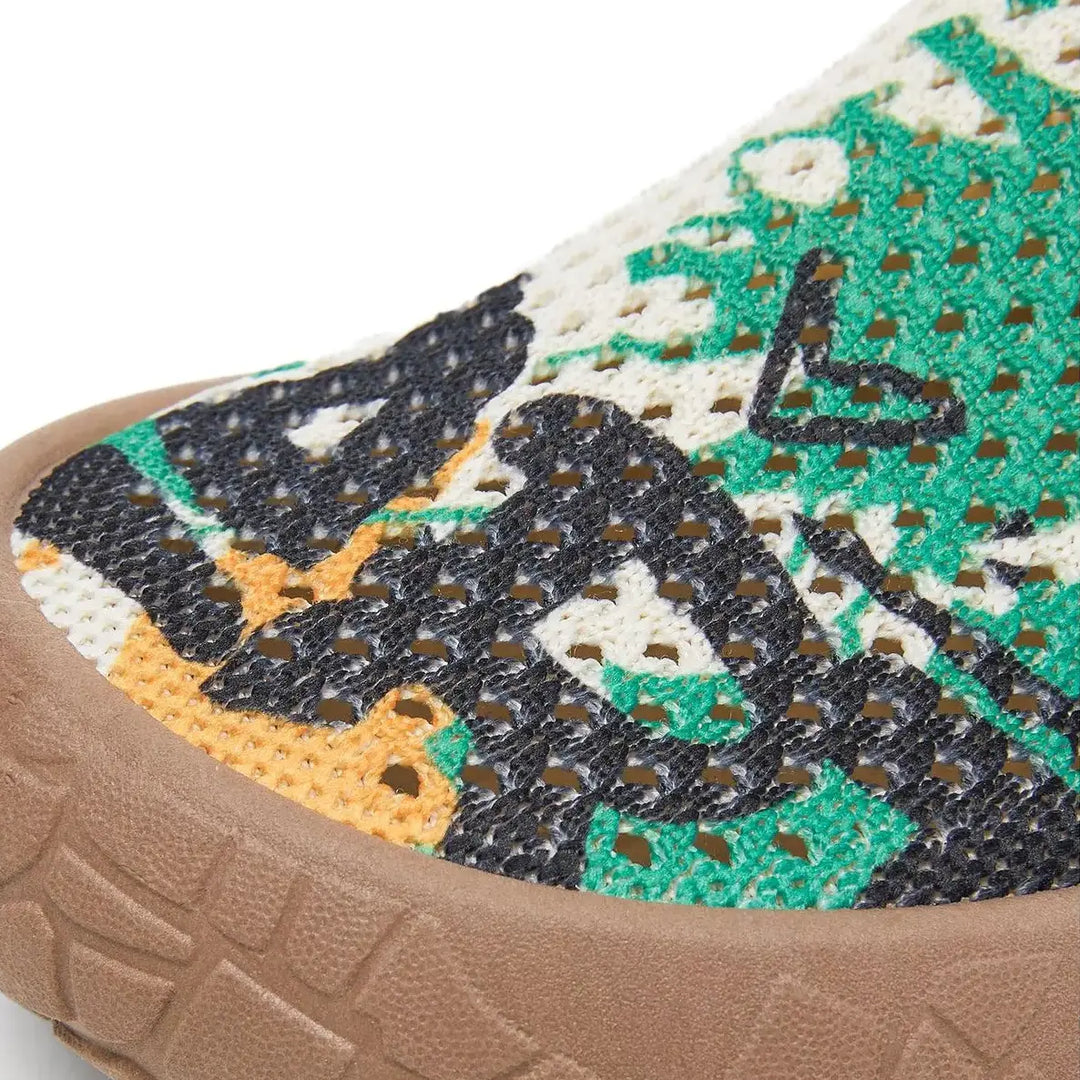 Close-up of Zyra artistic print slip-on flat shoe, showcasing the breathable fly-knit upper with a vibrant bohemian pattern in green, black, and yellow tones and a textured taupe sole.