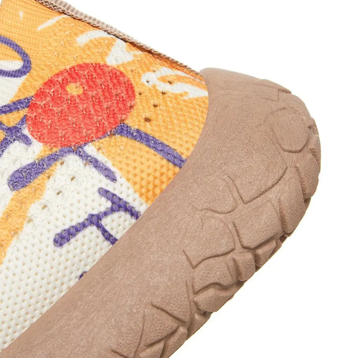 Close-up view of a slip-on flat shoe showcasing a vibrant artistic bohemian print on the breathable knit upper and a textured taupe rubber sole.