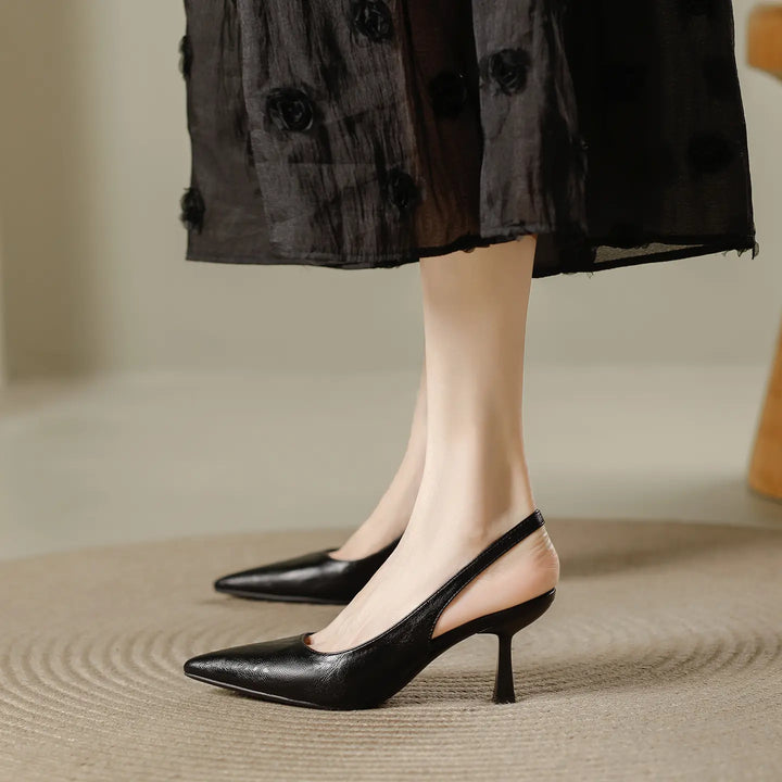 Elegant black pointed-toe slingback heels with a sculpted stiletto heel and thin elastic strap, worn with a textured black dress.