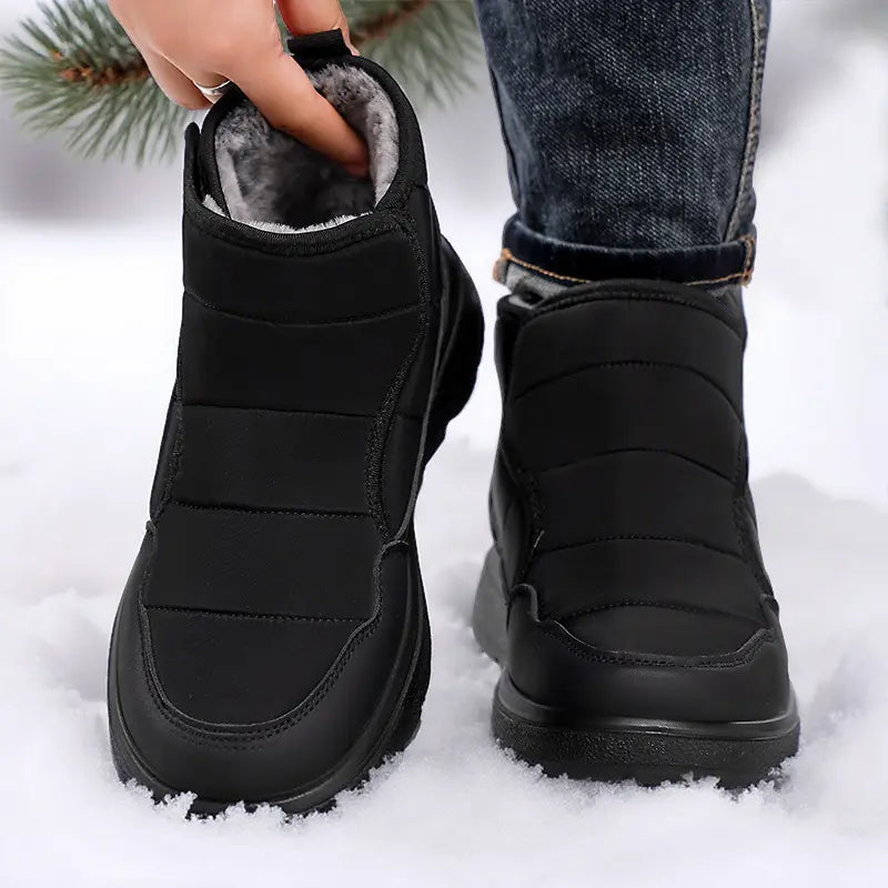 Men's Zyrkon black winter boots shown worn in the snow, featuring quilted puffer uppers, faux-fur lining, and velcro straps for easy on and off.