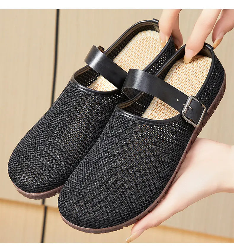Black breathable mesh slip-on loafers for women with an adjustable strap and metallic buckle, shown from the side on a neutral studio background.
